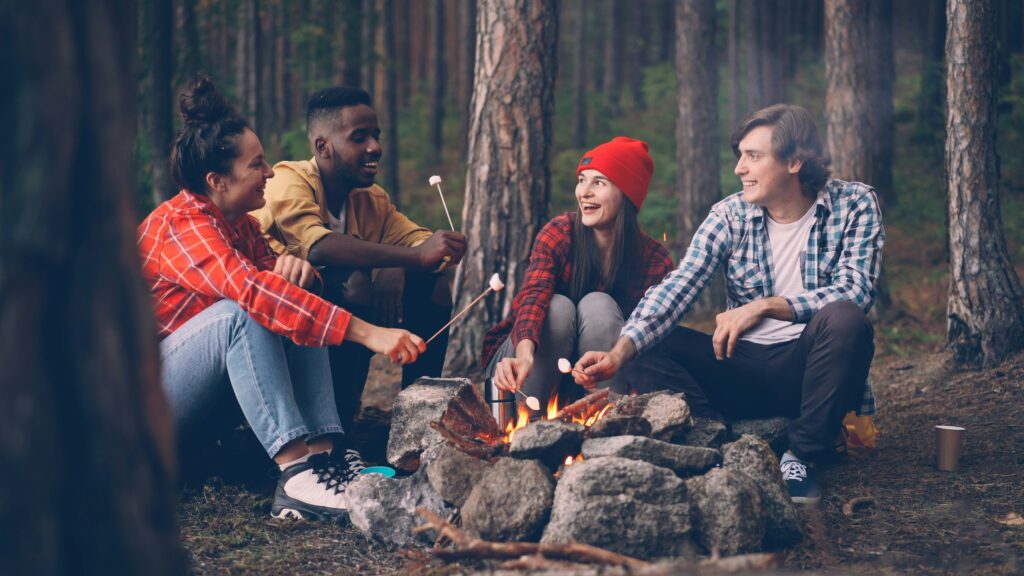 Four people sitting around a campfire enjoying roasting marshmellows.