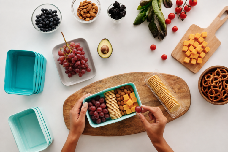 Hands holding a prepped container full of grapes, crackers, and cheese cubes.