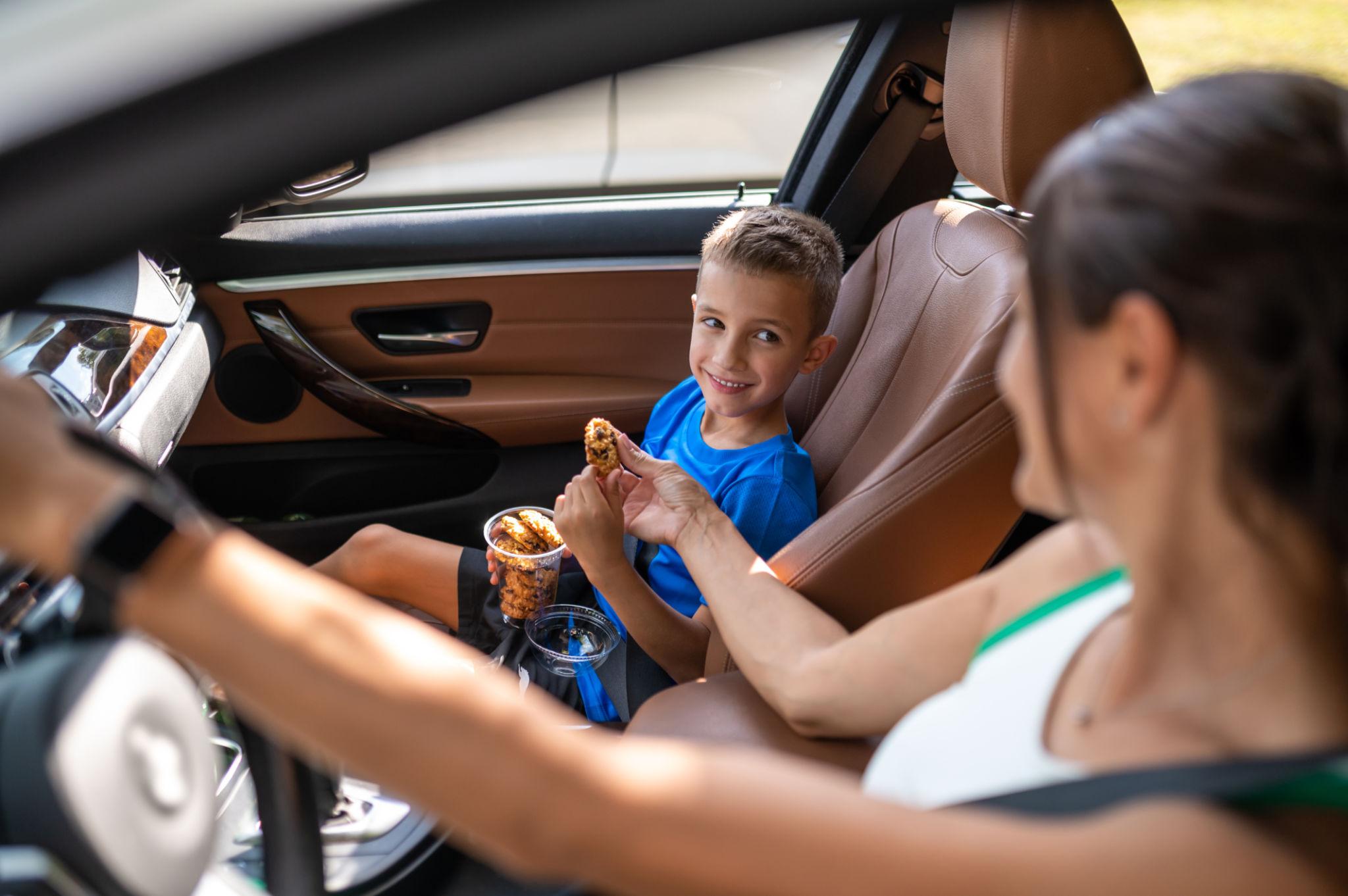 A mother in the drivers seat handing snacks to her son in the passenger seat.